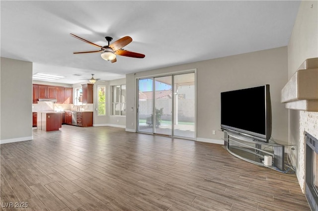 unfurnished living room featuring wood finished floors, ceiling fan, baseboards, and a fireplace