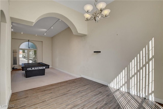 game room with baseboards, rail lighting, wood finished floors, and a notable chandelier