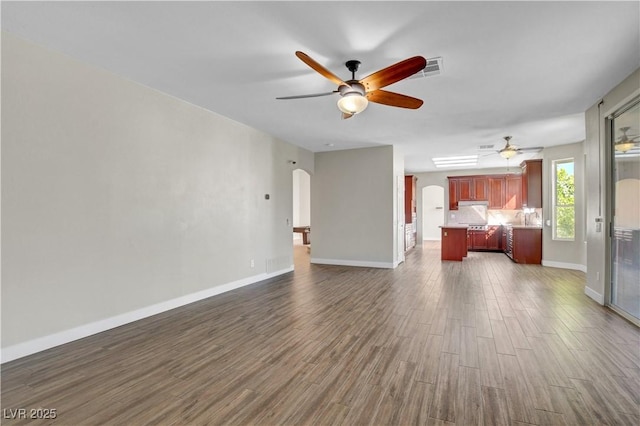 unfurnished living room featuring arched walkways, ceiling fan, baseboards, and dark wood-style floors