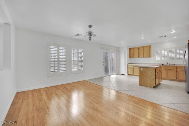unfurnished living room with baseboards, ceiling fan, a sink, and light wood-style flooring