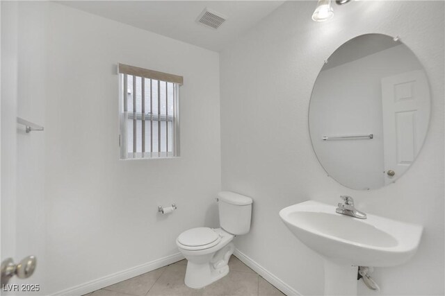 half bath with visible vents, toilet, baseboards, tile patterned floors, and a sink