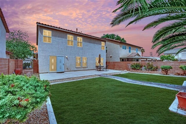 back of house at dusk featuring a lawn, a fenced backyard, a patio area, and stucco siding