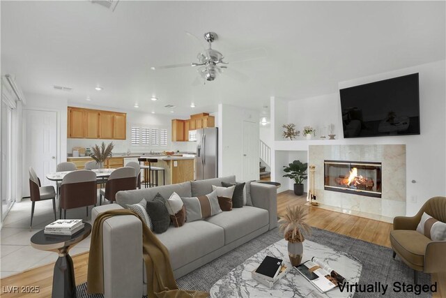 living room featuring stairs, recessed lighting, a ceiling fan, light wood finished floors, and a premium fireplace