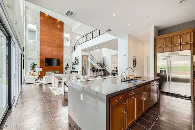kitchen with a kitchen island with sink, appliances with stainless steel finishes, a sink, open floor plan, and a high ceiling