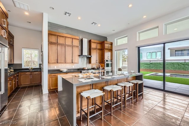 kitchen with wall chimney range hood, dark tile patterned floors, decorative backsplash, visible vents, and stainless steel oven