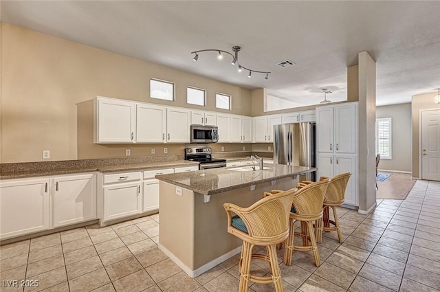1574 Livingston Dr, Henderson, NV 89012 - kitchen with stainless steel appliances, light tile patterned floors, white cabinets, stone counters, and an island with sink