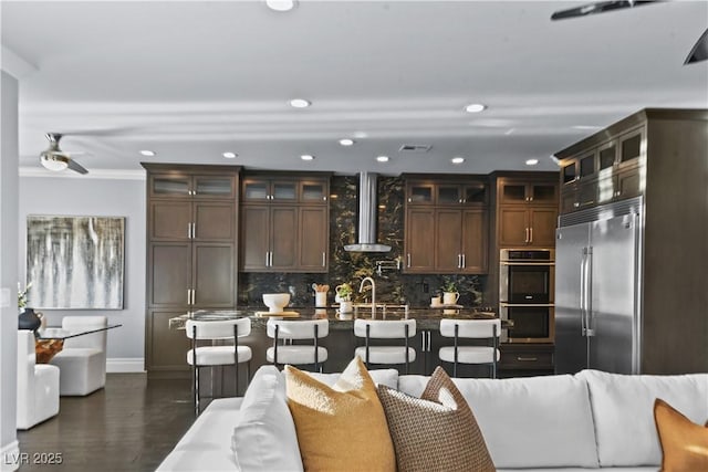 kitchen featuring wall chimney range hood, baseboards, appliances with stainless steel finishes, and decorative backsplash