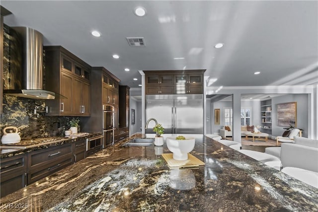 interior space with a sink, wall chimney exhaust hood, stainless steel appliances, recessed lighting, and visible vents