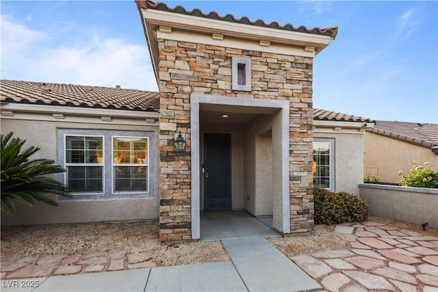 doorway to property featuring a tile roof, stone siding, and stucco siding