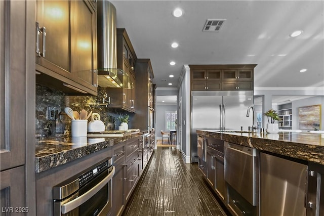 kitchen featuring visible vents, recessed lighting, dark stone counters, wall chimney exhaust hood, and stainless steel appliances