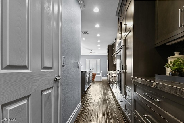 hall featuring visible vents, baseboards, dark wood-style floors, a textured wall, and recessed lighting
