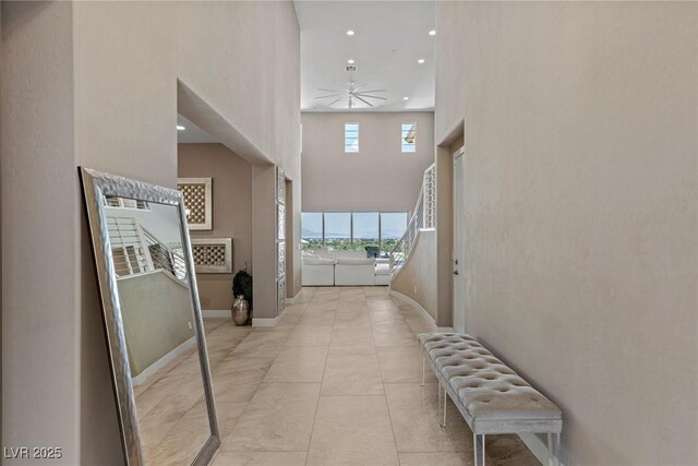 corridor featuring recessed lighting, baseboards, light tile patterned floors, and a towering ceiling