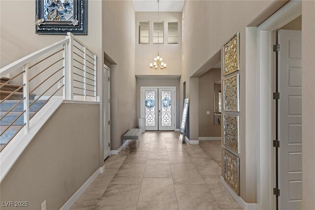 foyer entrance featuring french doors, a towering ceiling, a notable chandelier, baseboards, and marble finish floor