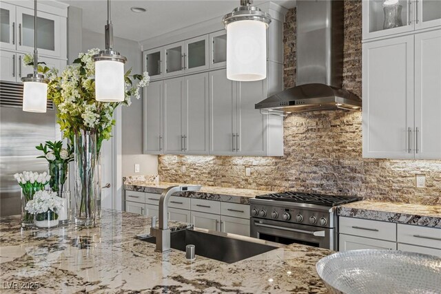kitchen featuring high quality appliances, wall chimney exhaust hood, light stone counters, a sink, and backsplash