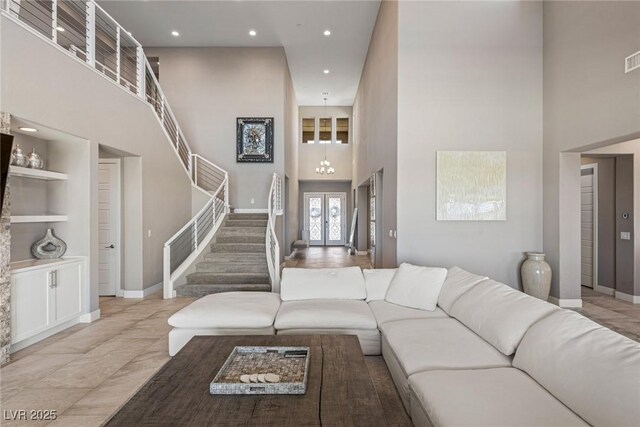 living area featuring french doors, a towering ceiling, built in features, stairway, and baseboards