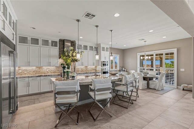 kitchen featuring appliances with stainless steel finishes, a kitchen island with sink, a healthy amount of sunlight, tasteful backsplash, and visible vents