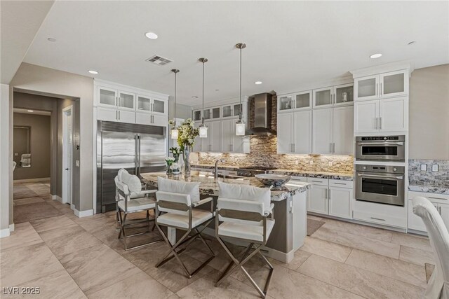 kitchen with wall chimney range hood, visible vents, tasteful backsplash, light stone counters, and stainless steel appliances