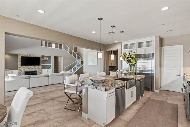 2 Olympia Outlook Dr, Las Vegas, NV 89141 - kitchen featuring appliances with stainless steel finishes, light stone countertops, white cabinets, a fireplace, and an island with sink