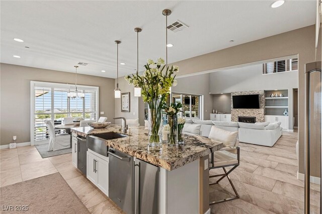 kitchen with light stone counters, a sink, a fireplace, a kitchen island with sink, and visible vents