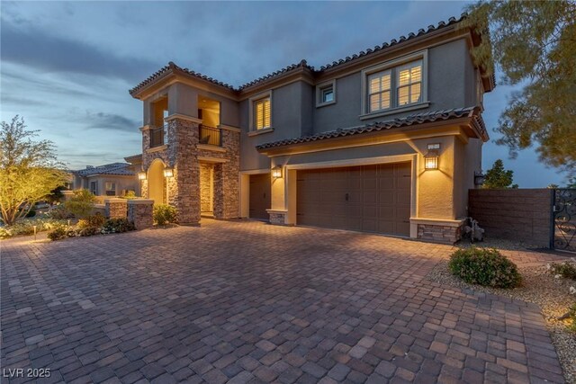 mediterranean / spanish home with decorative driveway, fence, an attached garage, stone siding, and stucco siding