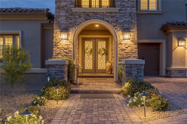 view of exterior entry featuring a garage, stucco siding, and stone siding