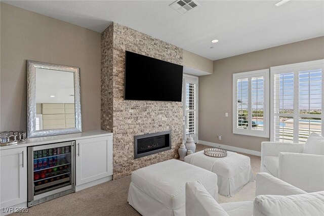 living area featuring visible vents, carpet flooring, wine cooler, and a stone fireplace