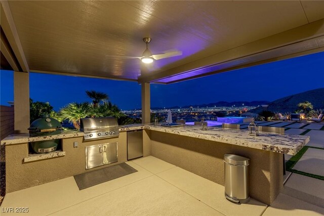 patio at twilight featuring ceiling fan, exterior kitchen, and a grill