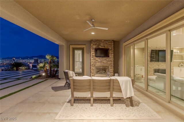 patio at twilight with a ceiling fan and an outdoor living space with a fireplace