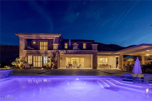 2 Olympia Outlook Dr, Las Vegas, NV 89141 - back of house at night featuring a balcony, a patio area, a tiled roof, an outdoor pool, and stucco siding