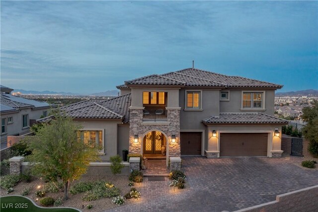mediterranean / spanish-style house featuring an attached garage, stucco siding, stone siding, and a tile roof