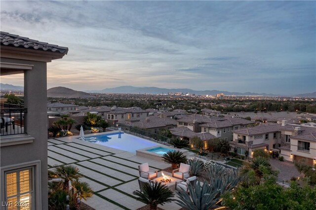 pool at dusk with a residential view, an outdoor pool, a mountain view, a patio, and a fire pit