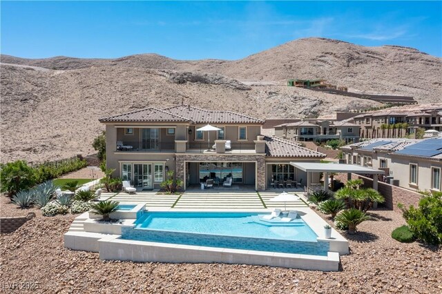 rear view of property with a tile roof, a mountain view, a balcony, stone siding, and stucco siding