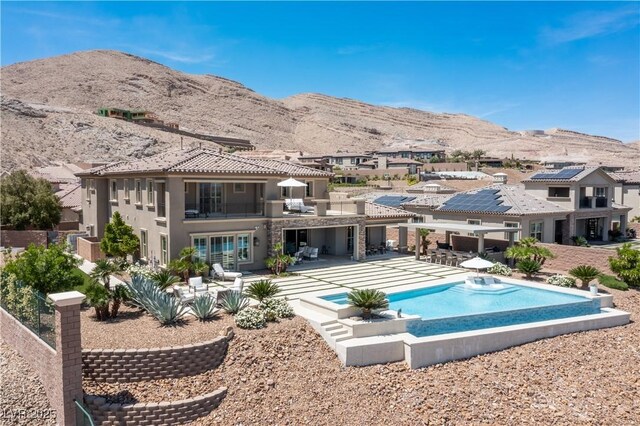 rear view of property with a mountain view, stucco siding, an outdoor pool, and a balcony