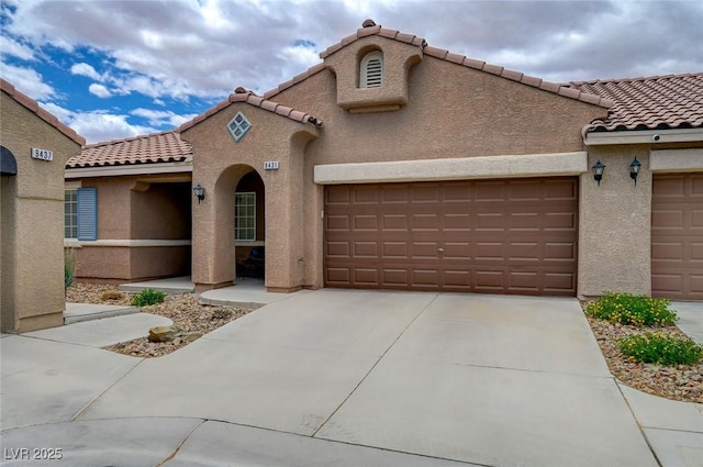 mediterranean / spanish-style house featuring a garage, stucco siding, a tile roof, and concrete driveway