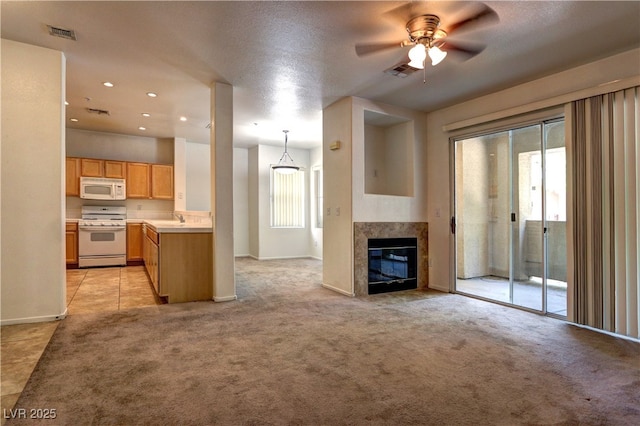 unfurnished living room with visible vents, ceiling fan, light colored carpet, a sink, and a premium fireplace