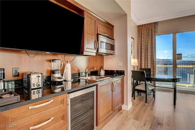 kitchen with crown molding, dark countertops, a sink, stainless steel microwave, and wine cooler