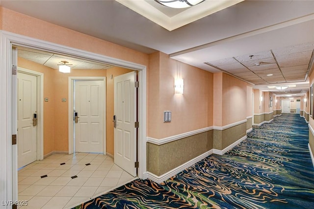 hallway with light tile patterned floors, baseboards, and light colored carpet