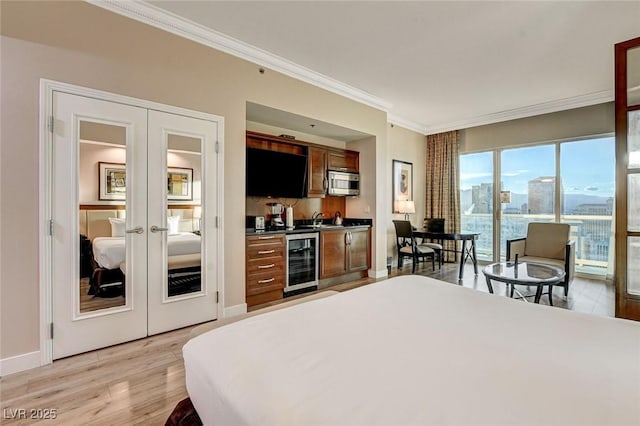 bedroom with light wood finished floors, beverage cooler, french doors, indoor wet bar, and ornamental molding