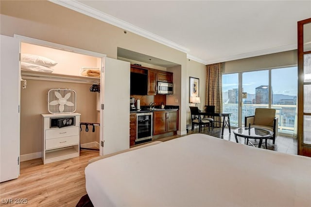 bedroom with wet bar, crown molding, light wood-type flooring, baseboards, and beverage cooler