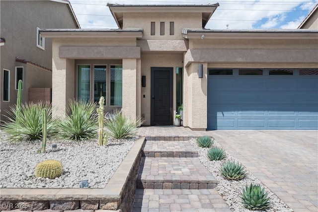 view of exterior entry featuring an attached garage, driveway, and stucco siding