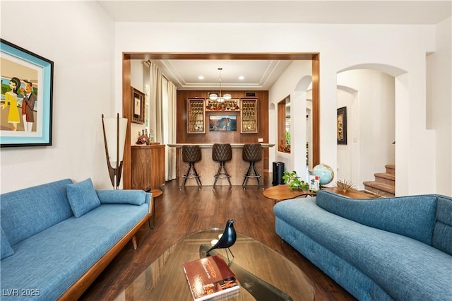living area with crown molding, a raised ceiling, arched walkways, stairs, and wood finished floors
