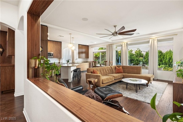 living room featuring a ceiling fan, visible vents, arched walkways, baseboards, and dark wood-type flooring