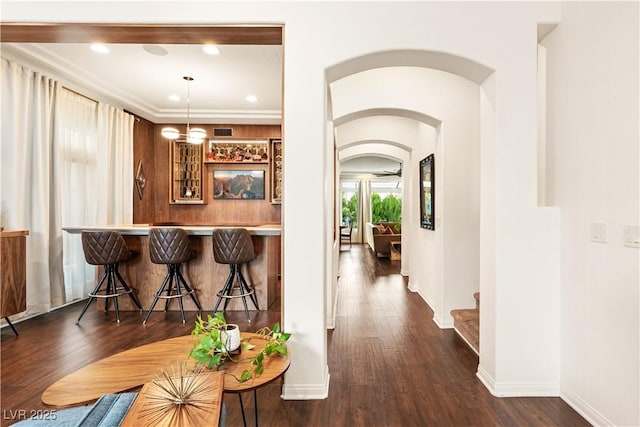 interior space with pendant lighting, arched walkways, baseboards, a bar, and dark wood-type flooring