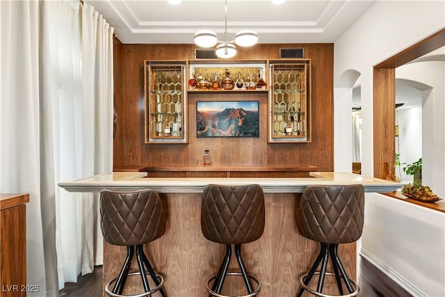 bar with wet bar, visible vents, arched walkways, a tray ceiling, and dark wood-type flooring