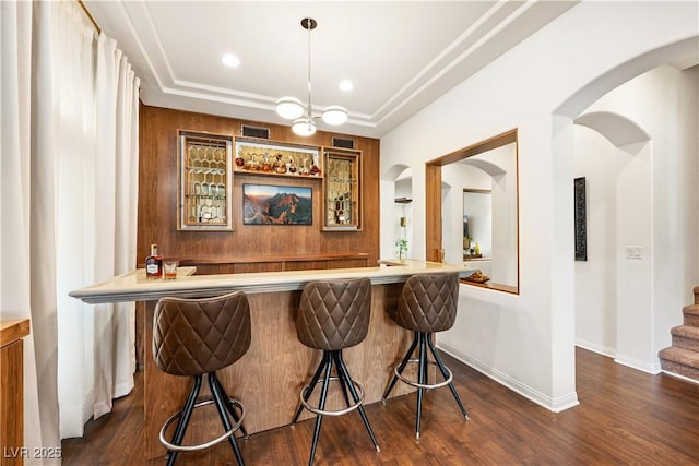 bar featuring baseboards, arched walkways, wet bar, and dark wood-style floors