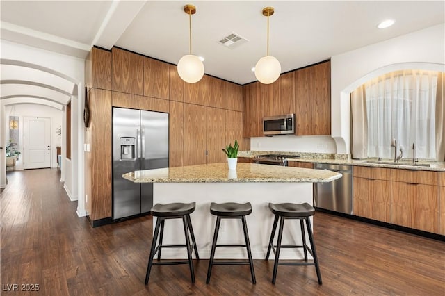 kitchen featuring a kitchen bar, visible vents, brown cabinets, a sink, and stainless steel appliances