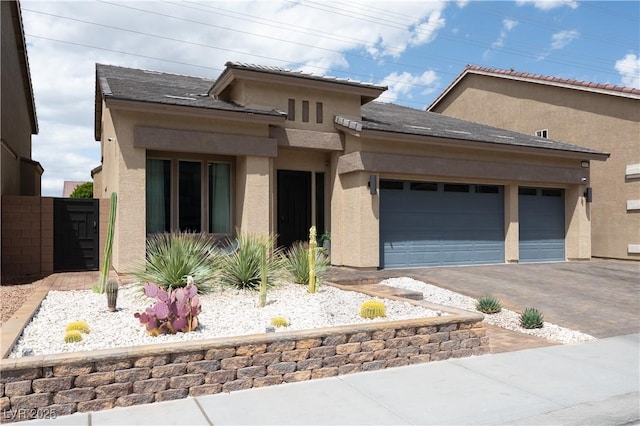 prairie-style home with fence, stucco siding, an attached garage, and driveway