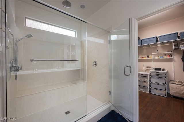 full bath with a spacious closet, a shower stall, and wood finished floors