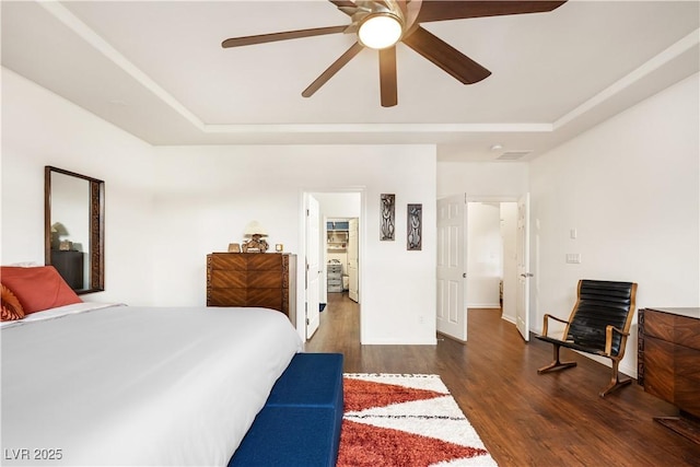 bedroom featuring ceiling fan, baseboards, wood finished floors, a tray ceiling, and visible vents