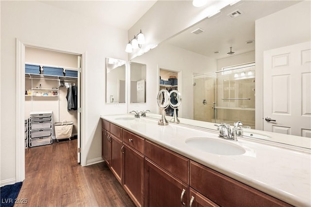 bathroom featuring a sink, a stall shower, wood finished floors, and visible vents
